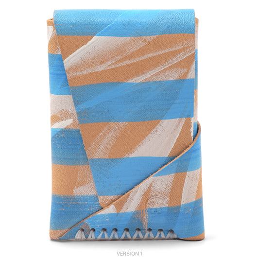 A folded leather card holder or sleeve with a textured finish, featuring a diagonal striped pattern in light blue, tan, and white, with a zigzag cut along the bottom edge, shown on a plain white background.