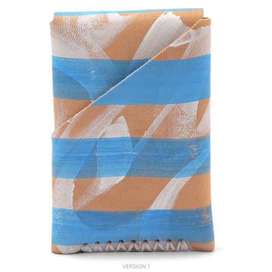A folded leather wallet or card holder featuring a modern abstract pattern of horizontal stripes in light blue, natural veg tan leather, and textured white, with a zigzag stitched edge at the bottom.