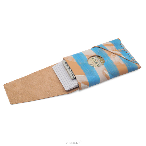 A handmade wallet made from scrap cardboard with a blue and tan striped pattern, featuring a slotted design and a visible dollar bill inside, shown on a white background.