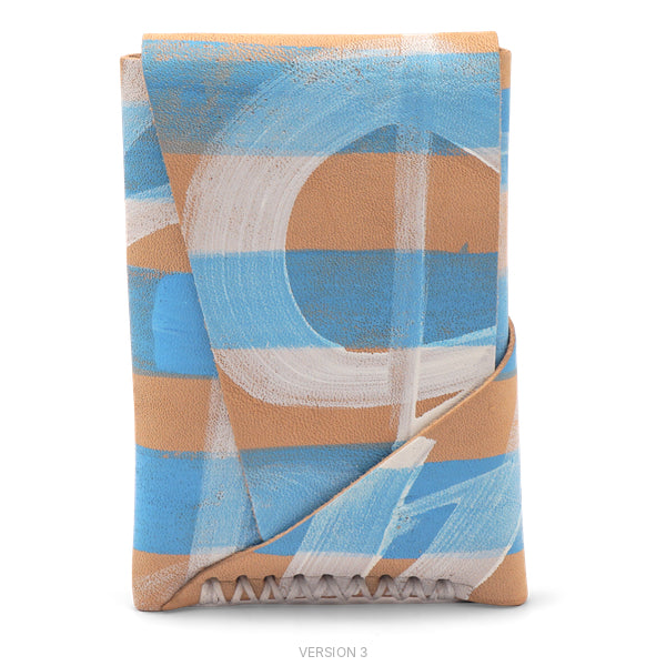A folded leather clutch or wallet with an abstract painted design in light blue, terracotta, and white, shown on a clean white background.